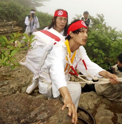 A devotee climbs up a chain path carrying a divine statue on his back.  (Japan News)