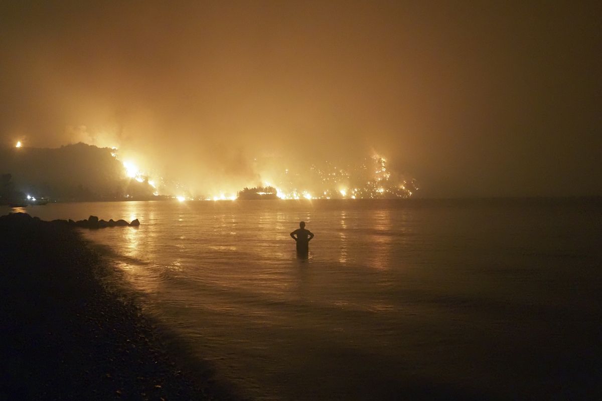 FILE - In this file photo dated Friday, Aug. 6, 2021, a man watches as wildfires approach Kochyli beach near Limni village on the island of Evia, about 160 kilometers (100 miles) north of Athens, Greece. A new massive United Nations science report is scheduled for release Monday Aug. 9, 2021, reporting on the impact of global warming due to humans.  (Thodoris Nikolaou)