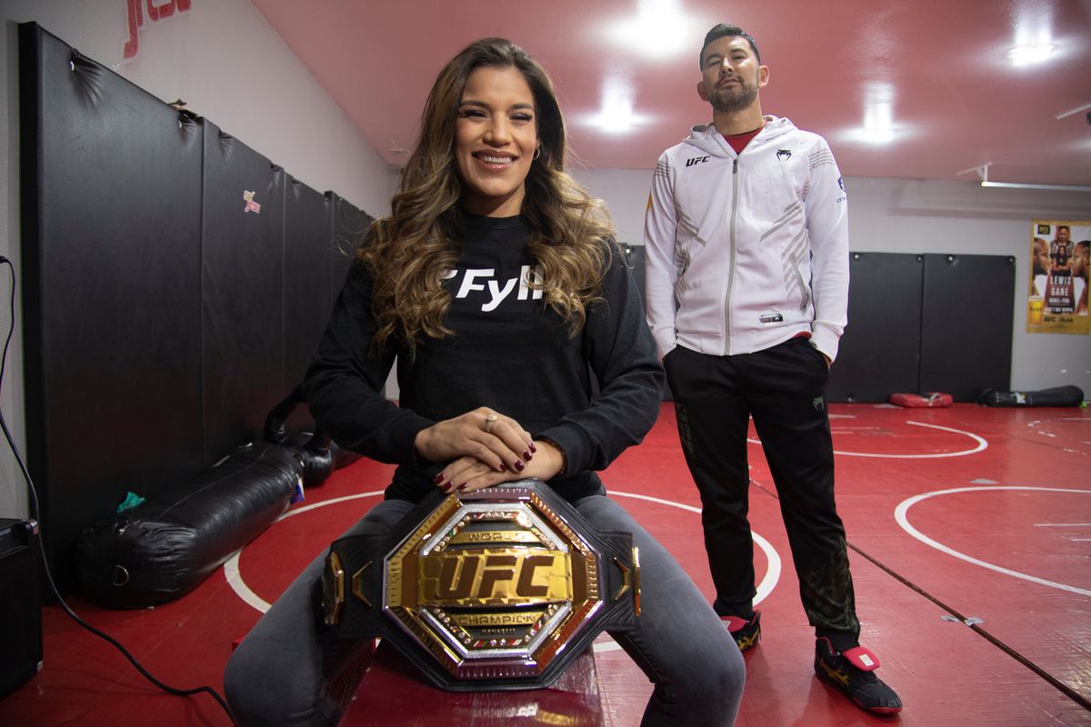 MMA fighter Julianna Peña, left, holds her recently won UFC title belt on Dec. 27 in her home gym in the Mead area, shortly after earning her title with a victory over Amanda Nunes in Las Vegas. At right is her coach, Rick Little.  (Jesse Tinsley/The Spokesman-Review)