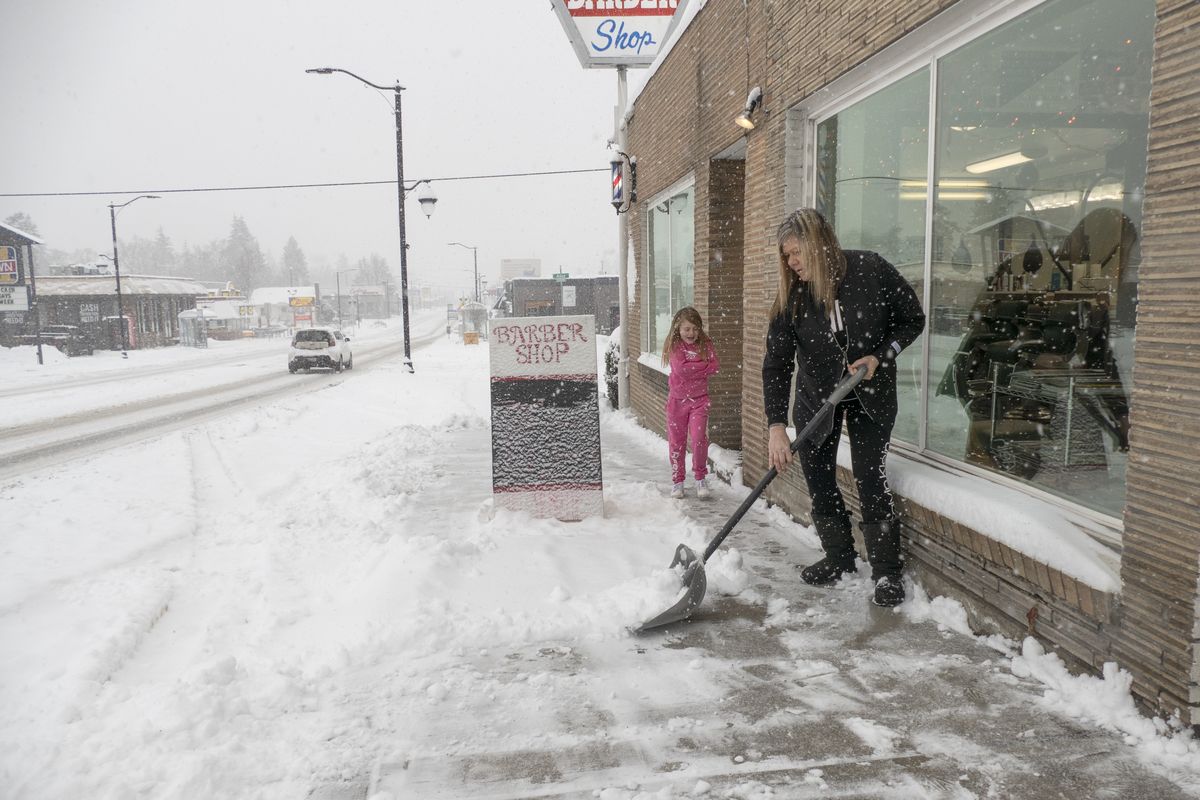 Six-year-old Brouke (cq) Rowley, left, watches her mom, Kokoe Rowley, a barber at Dan’s Barber Shop on North Monroe Street, clear the sidewalk Wednesday, Dec. 30, 2020, when several inches of snow fell in the morning and through the day.  (Jesse Tinsley/The Spokesman-Review)