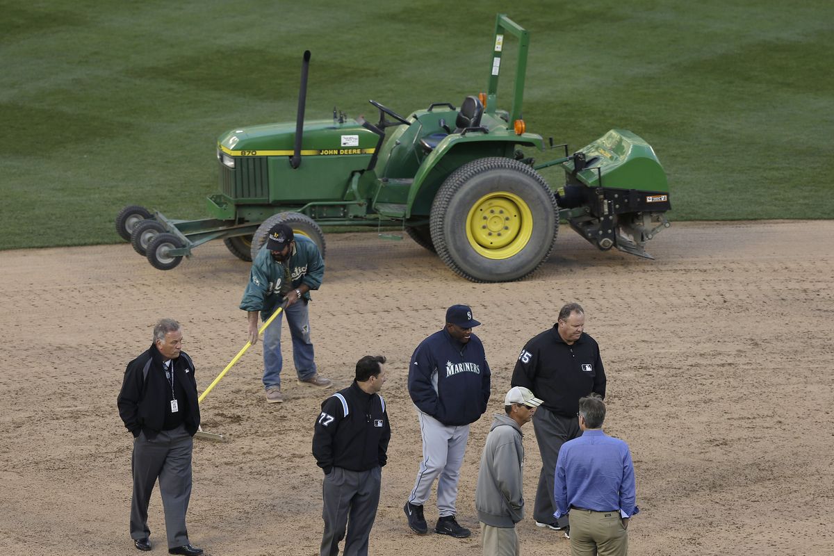 Seattle Mariners manager Lloyd McClendon, bottom center, turned his right ankle while examining the wet conditions out by shortstop. (Associated Press)