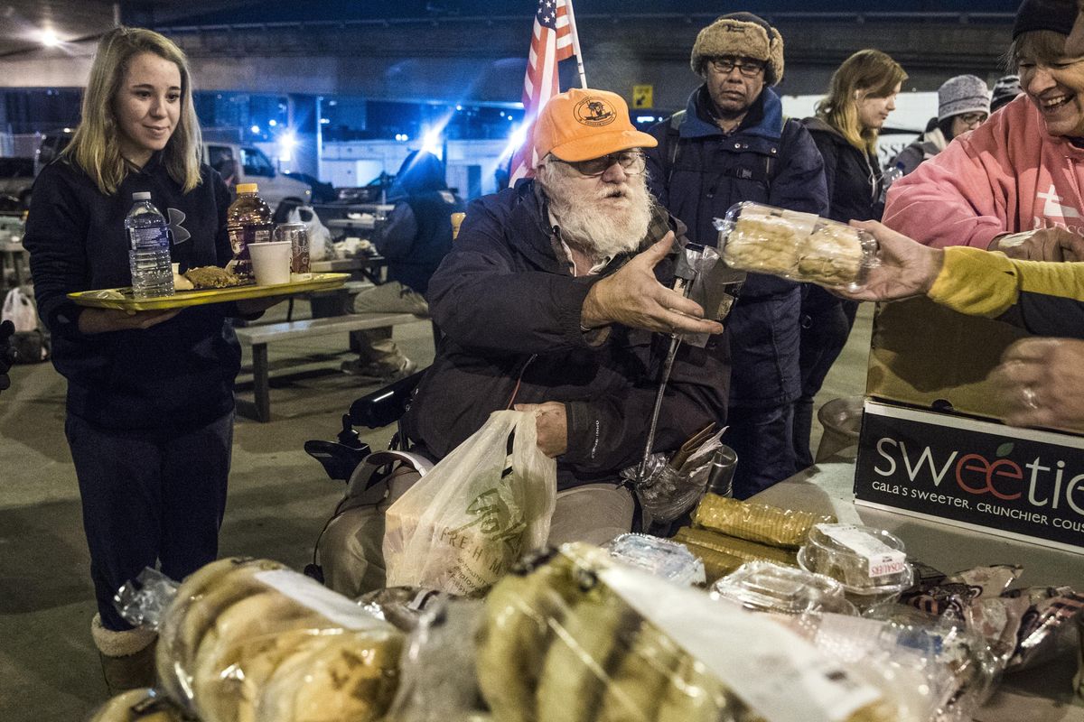 Joe Collins, 60, center, receives baked goods while attending the Blessings Under the Bridge, Wednesday, Nov. 15, 2017, in downtown Spokane, Wash. Volunteers Roxie Sundberg, 12, left, and Joanne Freeman, right, 55, help Collins through the line on the sidewalk near the corner of 4th Avenue and McClellan Street. (Dan Pelle / The Spokesman-Review)