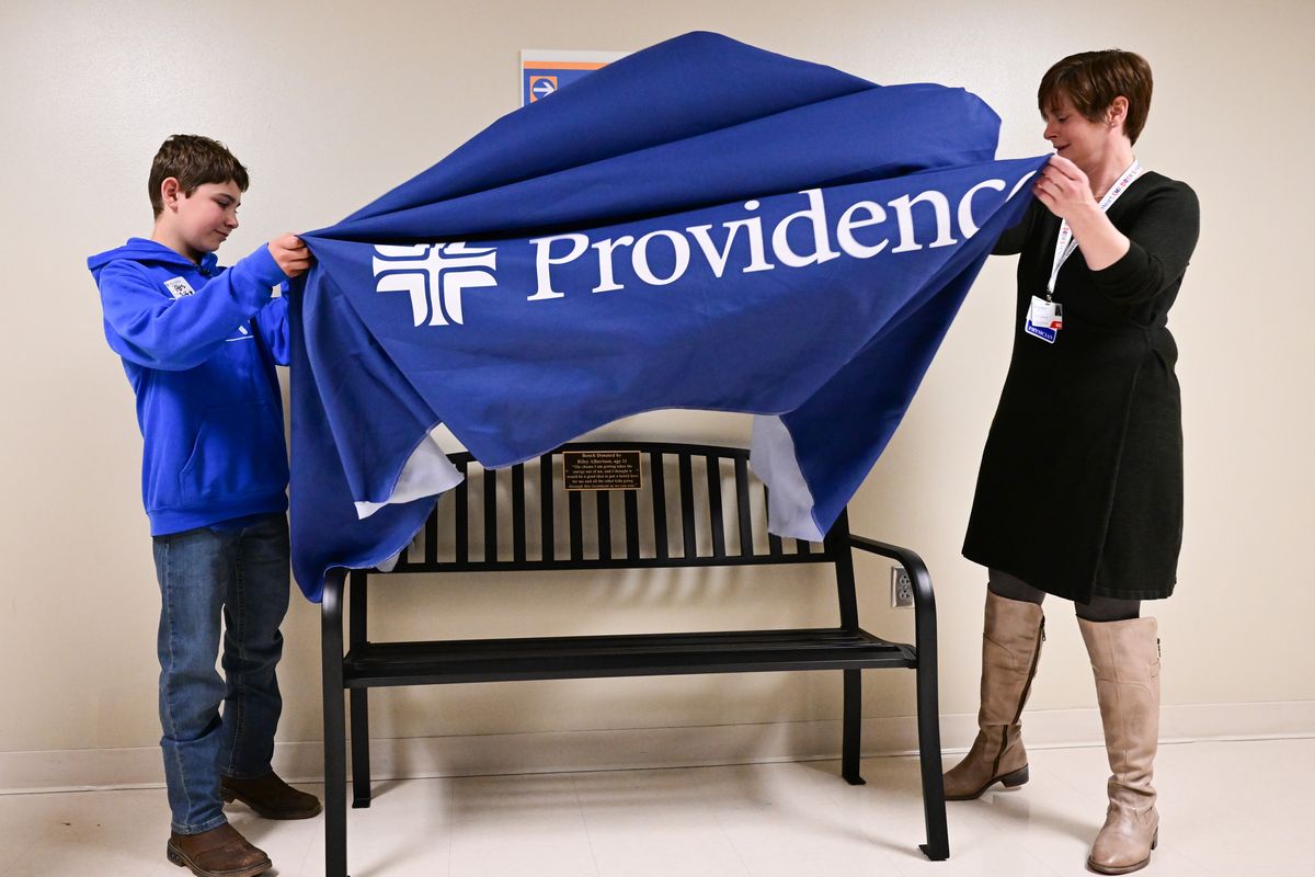 Cancer patient Riley Albertson, 11, left and Dr. Carrie Laborde, right, unveil a bench Albertson donated to the Providence Inland Northwest Foundation for children going through cancer treatment to rest between appointments on Friday, May 26, 2023, at Sacred Heart Children’s Hospital in Spokane, Wash.  (Tyler Tjomsland/The Spokesman-Review)