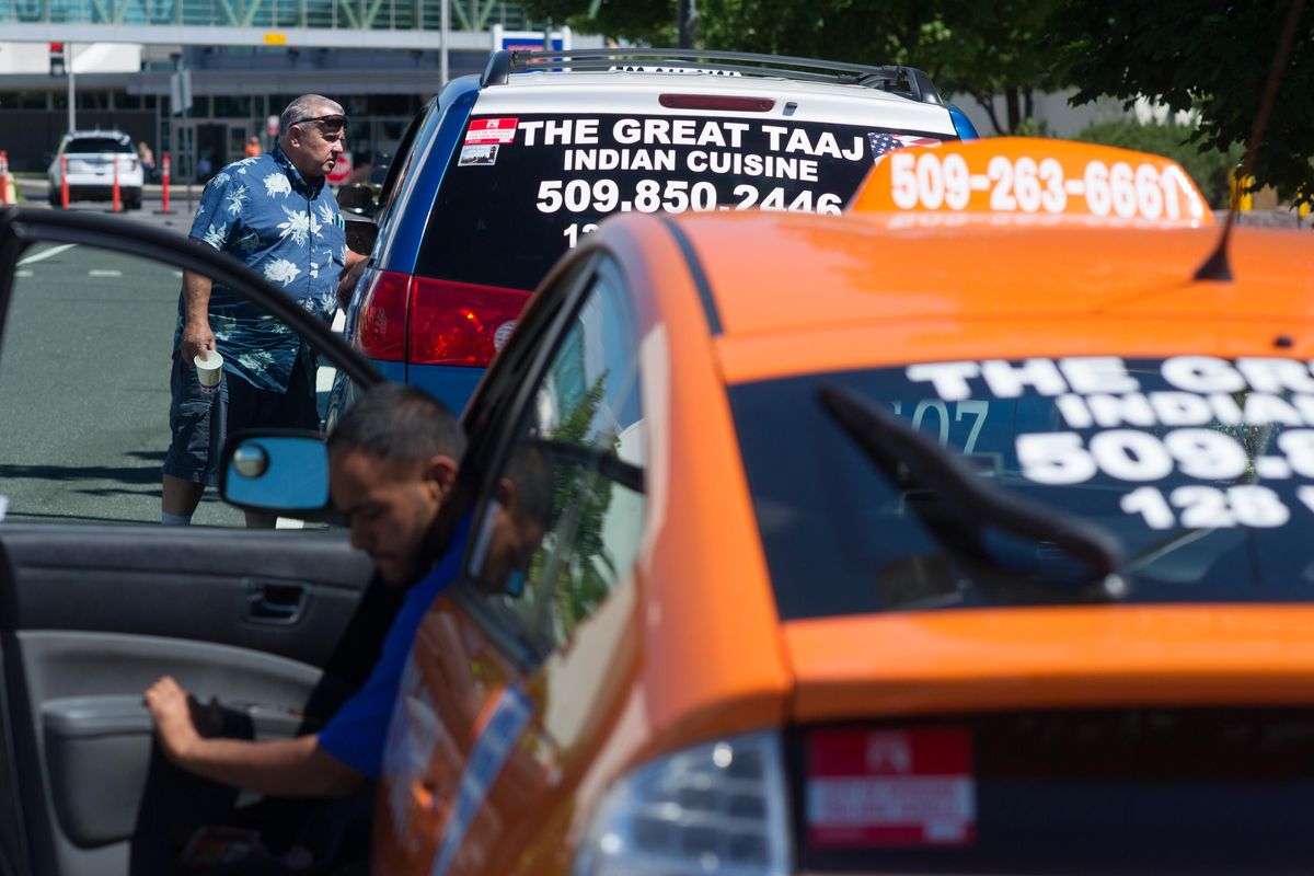 Luis Castillo, who owns Bull Dog cab company, top, chats with another driver waiting in the taxi queue, as Dagger Singh gets out of his cab on Friday, July 28, 2017, at Spokane International Airport in Spokane, Wash. (Tyler Tjomsland / The Spokesman-Review)