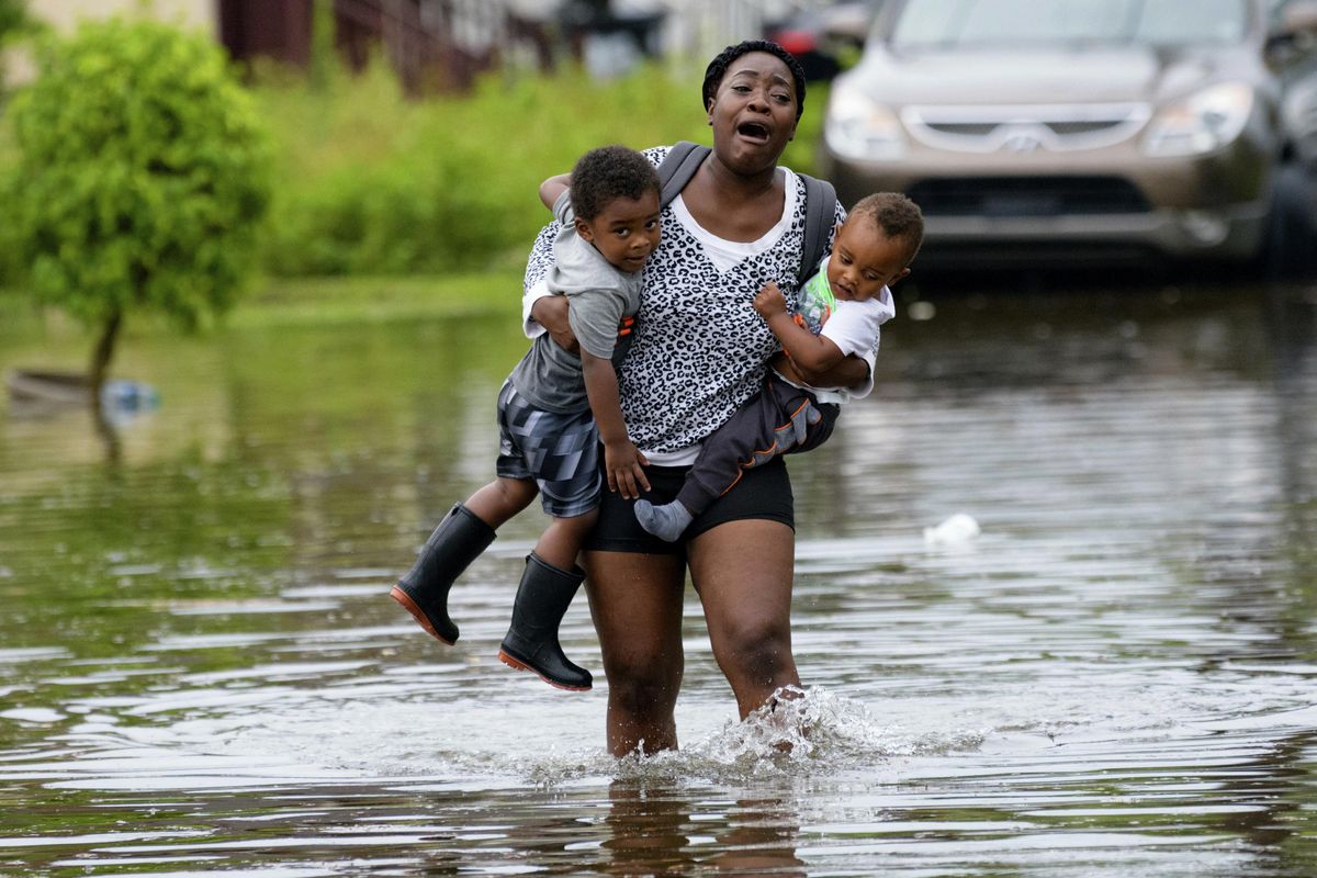 Terrian Jones reacts as she feels something moving in the water at her feet as she carries Drew and Chance Furlough to their mother on Belfast Street in New Orleans during flooding from a storm in the Gulf Mexico that dumped lots of rain Wednesday, July 10, 2019. (Matthew Hinton / AP)