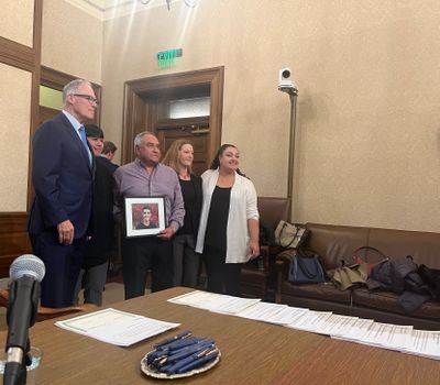 Sam Martinez’s family poses with Gov. Jay Inslee after he signed the bill sitting on the table before him. Hector Martinez, Sam’s father, holds a photo of Sam that the family brought. Standing next to Inslee is Sam’s cousin Ethan Morales, left, Martinez, mother Jolayne Houtz and sister Ariana Martinez-Lazo.  (Elena Perry/THE SPOKESMAN-REVIEW)