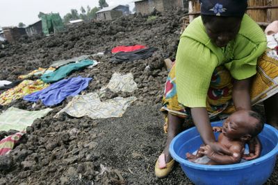 A woman bathes her baby next to laundry set out to dry on lava rock at a refugee camp Tuesday in Kibati,  in eastern Congo.  (Associated Press / The Spokesman-Review)