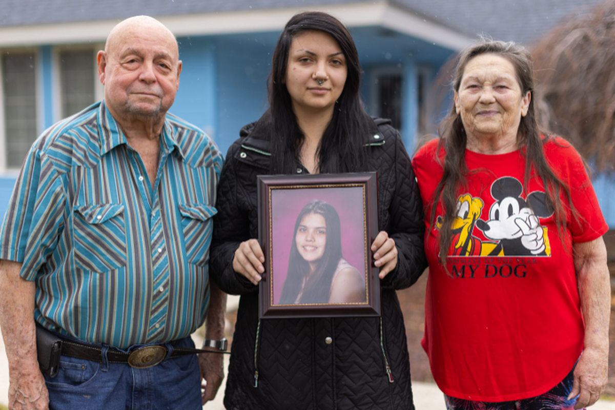 Charlie, left, Charlotte and Bonnie Groo stand outside the home where Kit Nelson-Mora was raised in Yakima, Wash. Charlotte holds a photo of Kit, who went missing at age 16.  (Jake Parrish/InvestigateWest)
