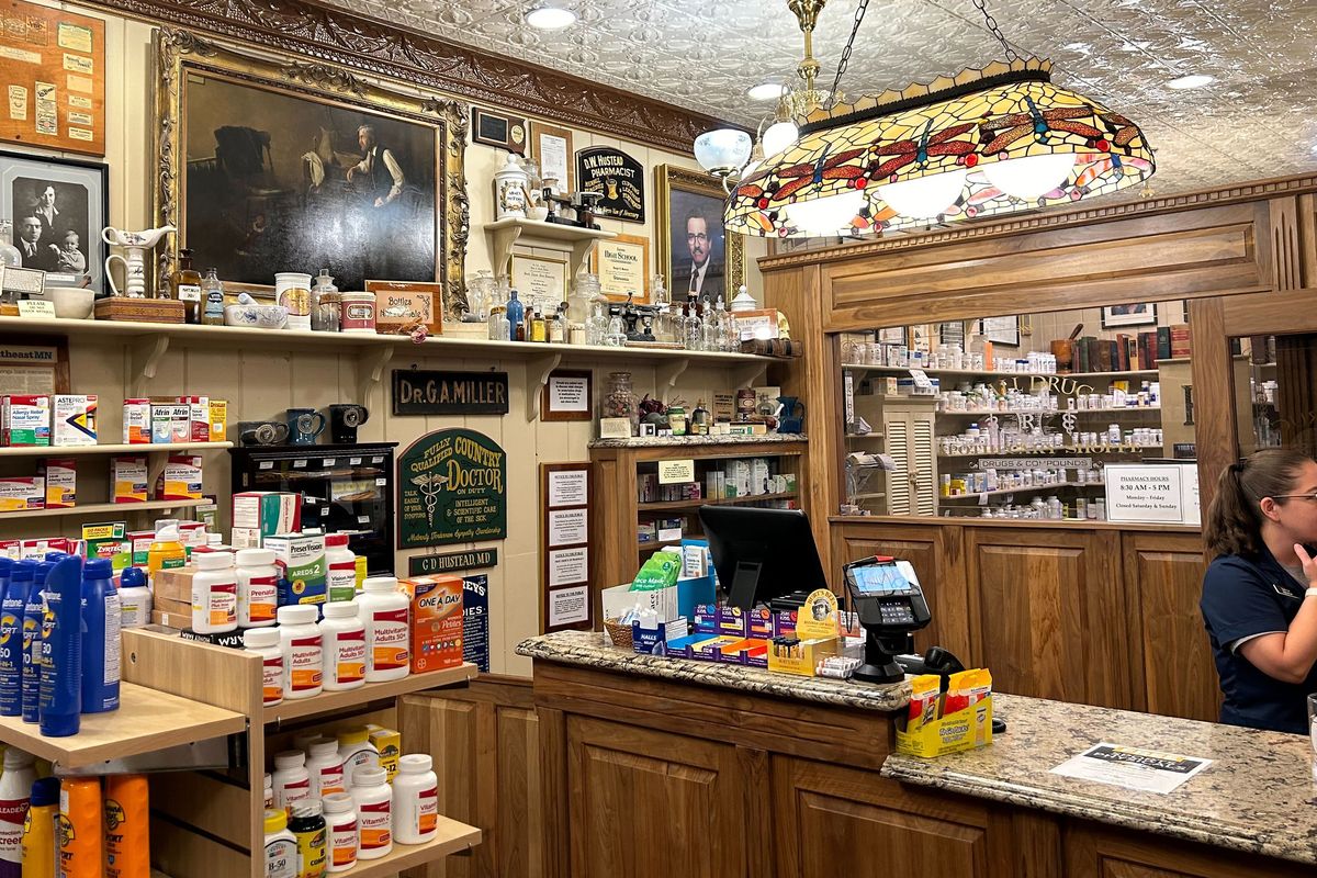 Sylvia Smith, the sole pharmacy tech at Wall Drug, works behind a wooden counter. Shelves display vintage equipment alongside modern medicine.   (Arielle Zionts/KFF Health News/TNS)