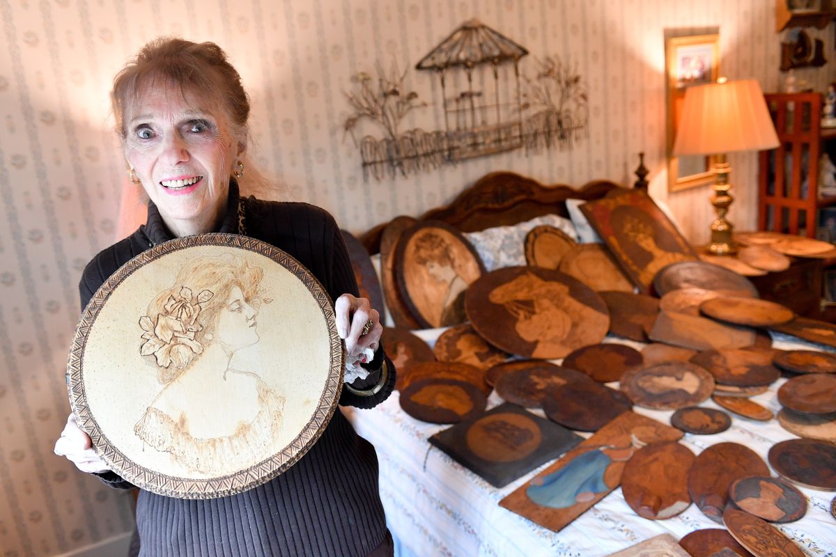 Marilyn Akerhielm poses for a photo with one of her favorite pyrographic plaques on June 13 at her Spokane home.  (Tyler Tjomsland/The Spokesman-Review)