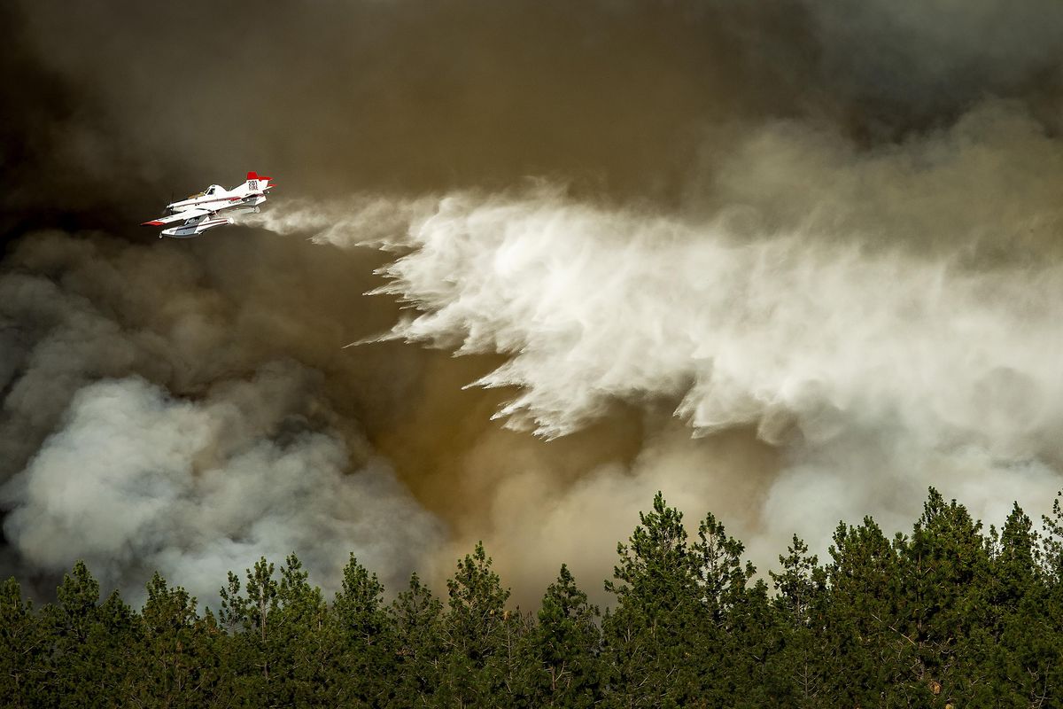 A fire fighting aircraft makes a water drop on a wildfire approaching a house on the East 6500 block of East Valley Springs Road Tuesday evening. Fire crews fought a fast-moving wildfire just north of Upriver Drive that has engulfed at least one home and prompted fire officials to call for a level-three evacuation for homeowners in the area. (Colin Mulvany / The Spokesman-Review)