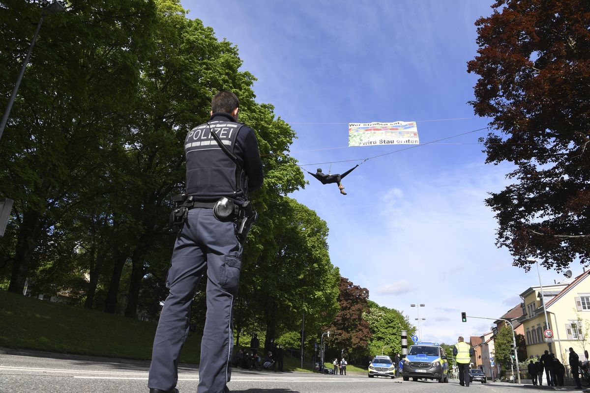 A climate activist hangs on a rope above the federal highway 32, above him a poster "Who sows roads, will reap traffic jams" in Ravensburg, Germany, Saturday, May 15, 2021. The road has been closed for hours. The police are preparing to clear the road and take the activists down.  (Felix Kaestle)