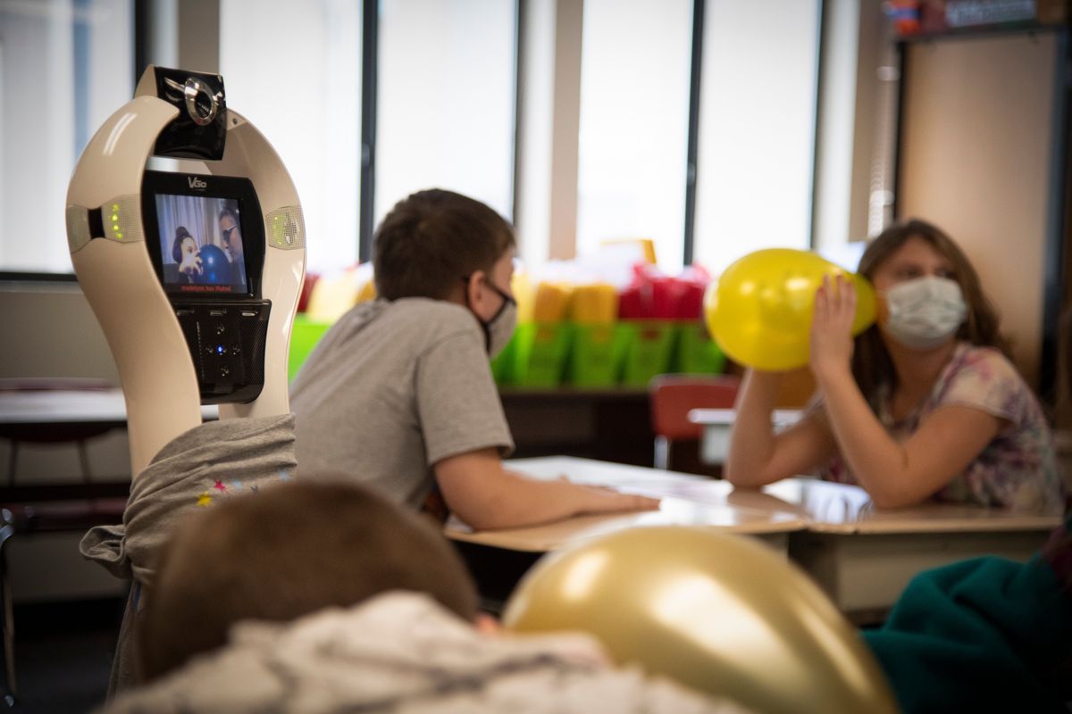 While other fourth-graders learn about sound waves by listening through a balloon, fourth-grader Madelyn Schible is seen on the screen of her robot, at left, doing the same exercise with her mother at home during class at Madison Elmentary School on Monday. Using the camera on her robot, Madelyn can steer through the hallways to get from class to class. Because of cerebral palsy, she is medically fragile and uses the robot, provided by Wishing Star Foundation, to go to school. The camera above her screen can be tilted up and down while she drives the robot to class.  (Jesse Tinsley/THE SPOKESMAN-REVI)