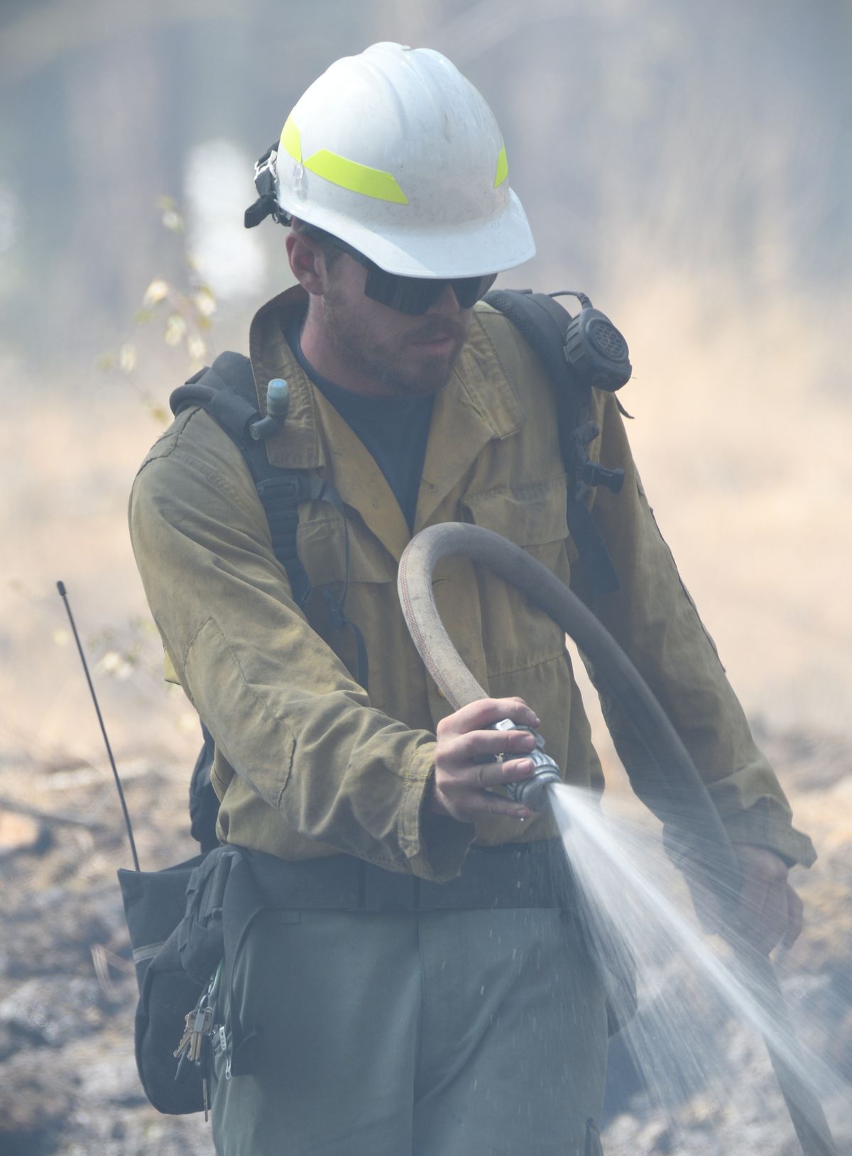 A firefighter douses hot spots left from a small brush fire Sunday near Cheney.  (COLIN TIERNAN/THE SPOKESMAN-REVIEW)