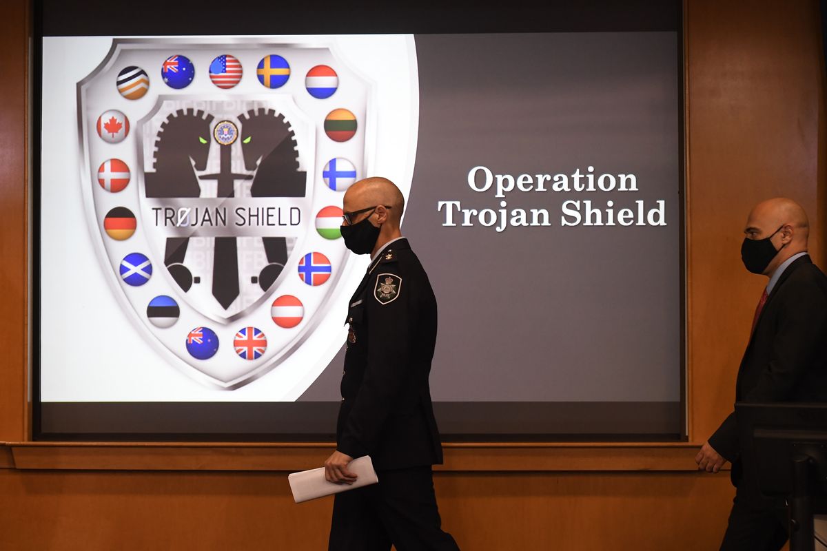 Law enforcement officials walk past an Operation Trojan Shield logo at a news conference, Tuesday, June 8, 2021, in San Diego. The global sting operation involved an encrypted communications platform developed by the FBI and has sparked a series of raids and arrests around the world in which more than 800 suspects were arrested and more than 32 tons of drugs – cocaine, cannabis, amphetamines and methamphetamines were seized.  (Denis Poroy)