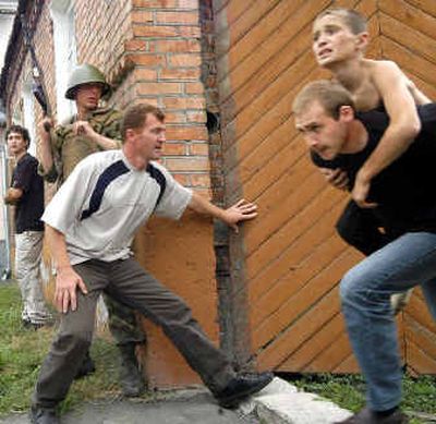 
A man carries a boy hostage as a soldier and volunteer stand behind a school fence during the rescure operation in the town of Beslan, North Ossetia. Six loud explosions could be heard outside the school within the space of about 15 minutes, and shortly afterward it was reported that some hostages had escaped. 
 (AFP/Getty Images / The Spokesman-Review)