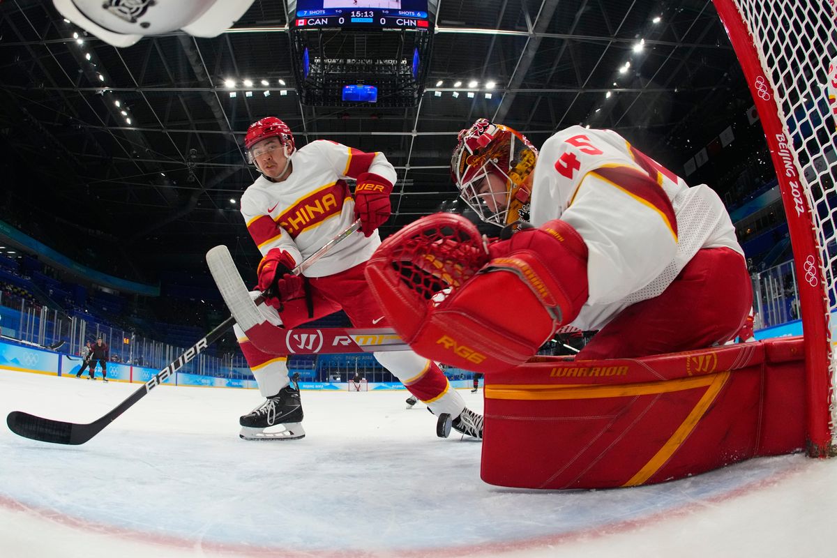 China goalkeeper Jeremy Smith reaches for the puck as Jason Fram watches during a men’s qualification-round hockey game against Canada at the 2022 Winter Olympics, Feb. 15 in Beijing.  (Associated Press)