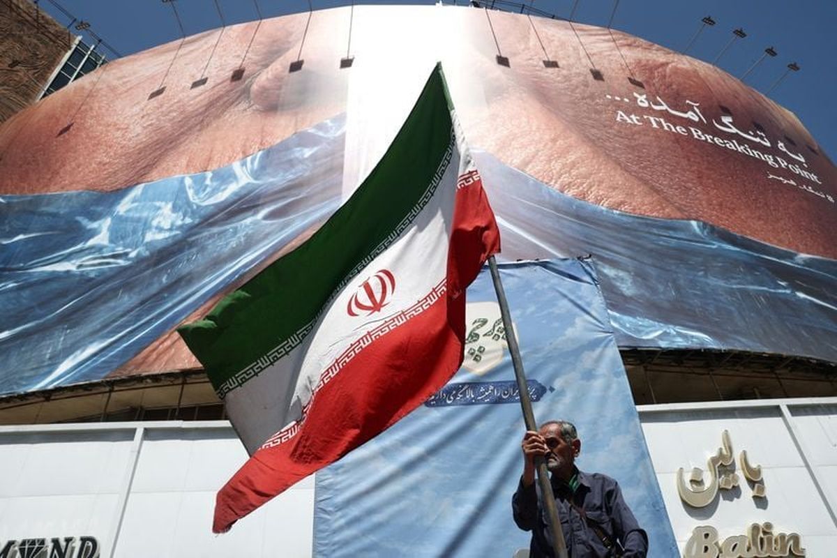 A man holds an Iranian flag near an anti-U.S. billboard depicting U.S. President Donald Trump and the Strait of Hormuz on Saturday, in Tehran, Iran. (Reuters )