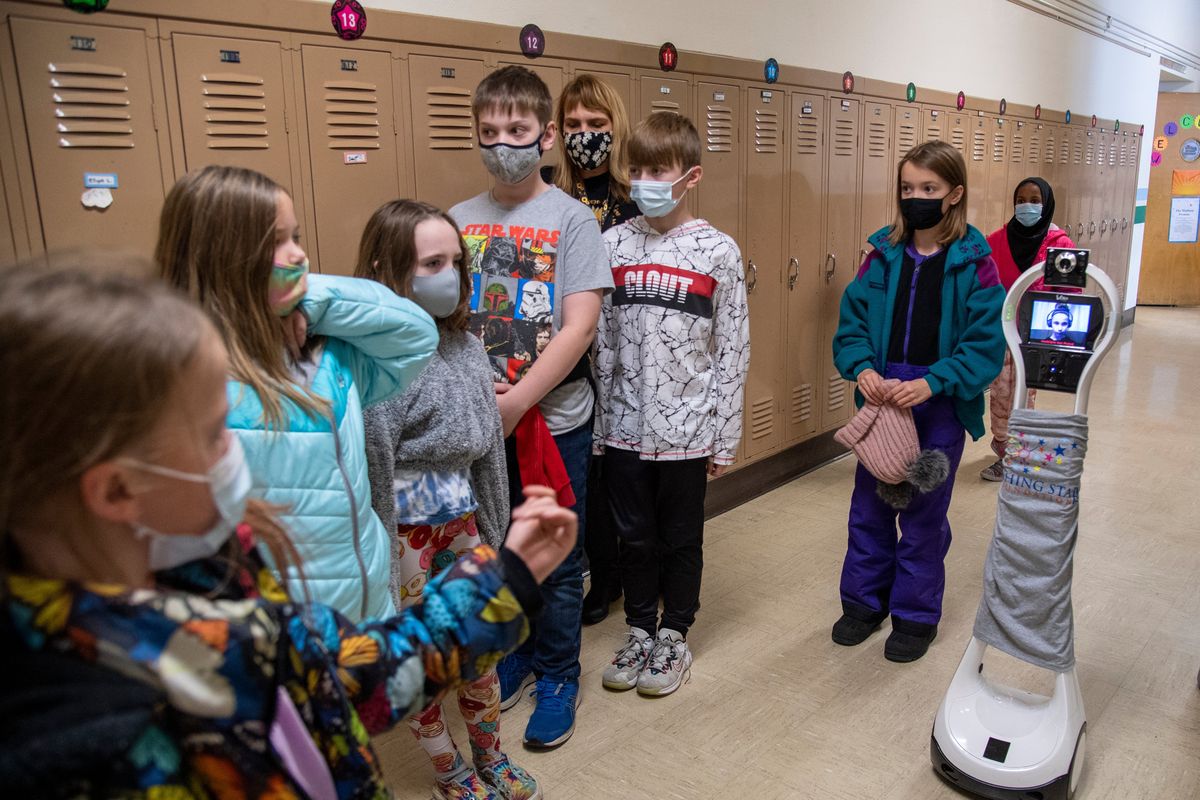 Classmates wait while fourth-grader Juliet McLemore, (holding hat), performs the duties of “bot buddy” and looks out for obstacles while she walks beside classmate Madelyn Schible, right, who appears on the tiltable screen of her “robot” while it rolls through the halls at Madison Elementary School on Monday in Spokane. Schible is able to attend school via the robot.  (Jesse Tinsley/THE SPOKESMAN-REVI)