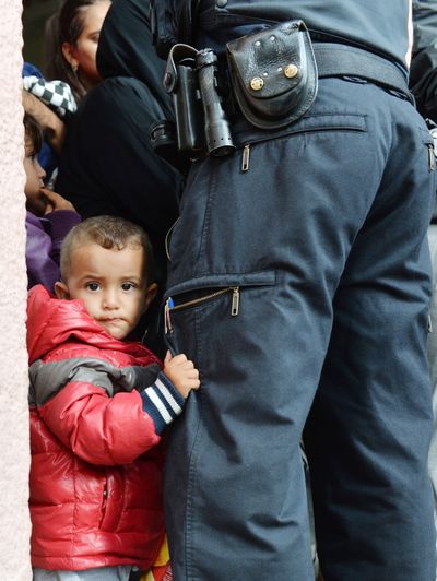 A young refugee holds the leg of a policeman as he waits for the registration at the rail station in Freilassing, Germany, on Tuesday. (Associated Press)