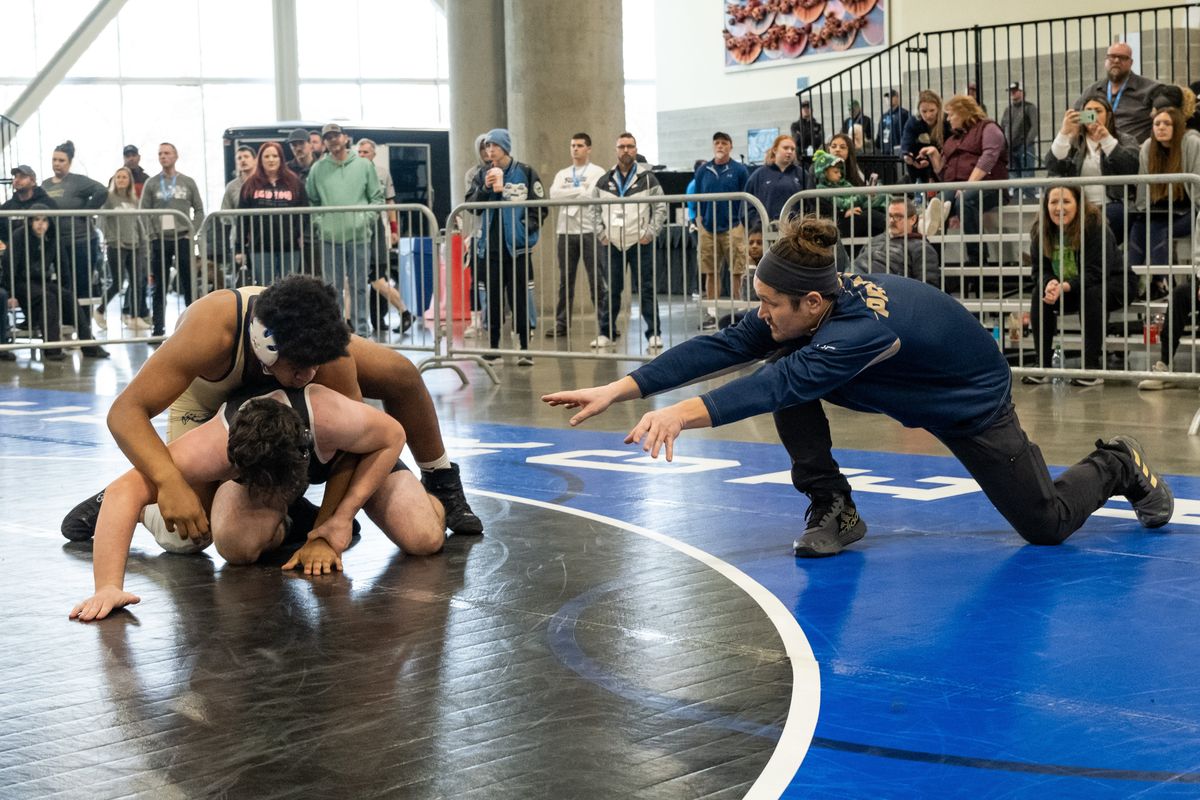 Mead interpreter Derek Hardin, right, signs instructions to Keemani Benavides, top, during the Greater Spokane League district wrestling tournament.  (Madison McCord/For The Spokesman-Review)