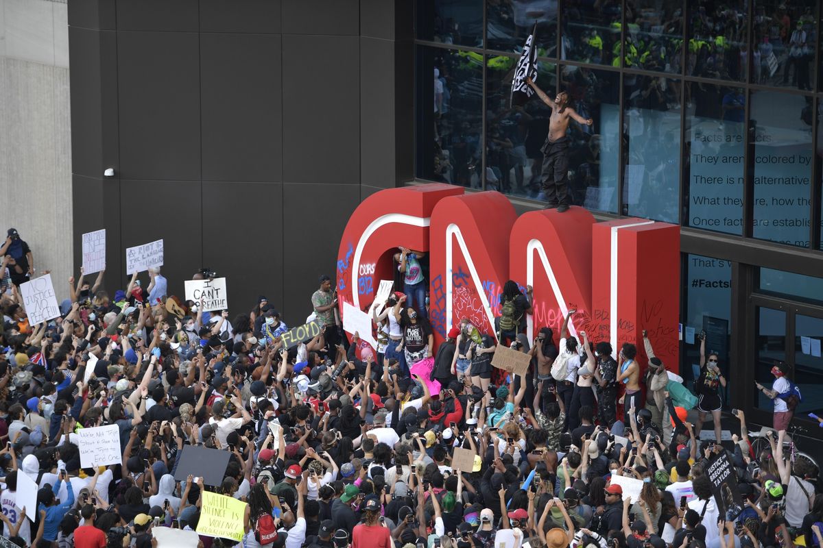 Demonstrators paint on the CNN logo during a protest march, Friday, May 29, 2020, in Atlanta, in response to the Memorial Day death of George Floyd in police custody in Minneapolis. The protest started peacefully earlier in the day before demonstrators clashed with police. (Mike Stewart / Associated Press)