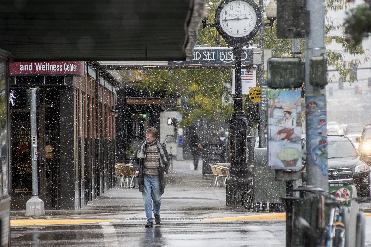 FILE - In this Sept. 29, 2019 file photo, a pedestrian crosses Front Street under snowfall in Missoula, Mont. Lawmakers are trying to stop 144 cities across the U.S. from losing their designations as “metropolitan areas” because the federal government is upgrading the standard from a minimum of 50,000 residents in its core to a minimum of 100,000 people. Missoula is among those at risk of losing the designation.  (Ben Allan Smith)