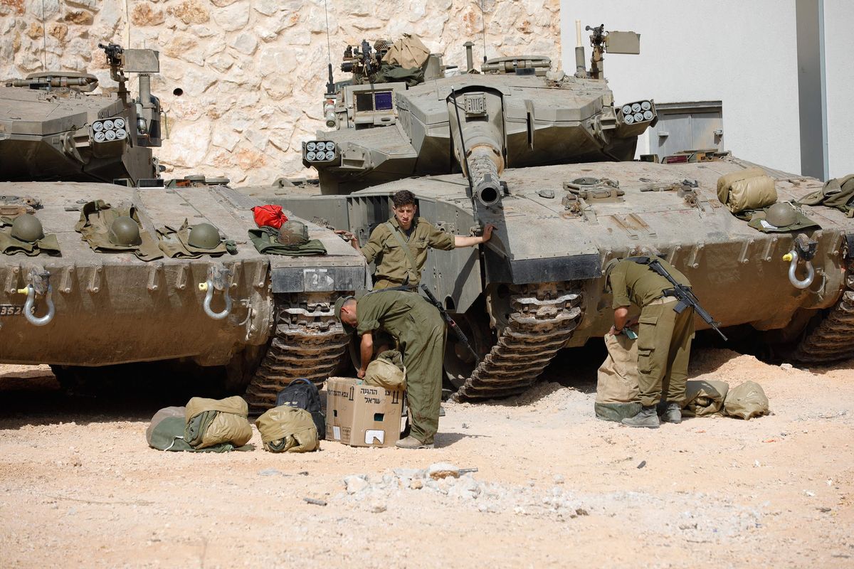 Israeli soldiers make preparations in front of Merkava tanks as they man a position at an undisclosed location on the border with Lebanon on Sunday.  (JALAA MAREY/AFP)