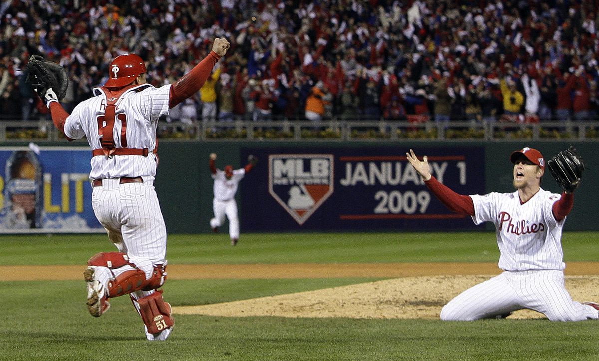 Phillies catcher Carlos Ruiz rushes toward closer Brad Lidge, who kneeled after saving Game 5 with a scoreless ninth inning.  (Associated Press / The Spokesman-Review)