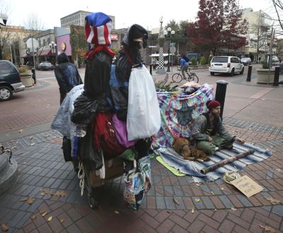 In a Nov. 10, 2016 photo, a visitor hauls a cart full of belongings through downtown Eugene, left, past another visitor asking for money at Broadway and Willamette in Eugene, Ore. A wave of complaints about aggressive dogs in the downtown area of Oregon's third most populous city has prompted Eugene city councilors to ban dogs from the downtown area except those owned by people who live or work there. (Chris Pietsch / AP)