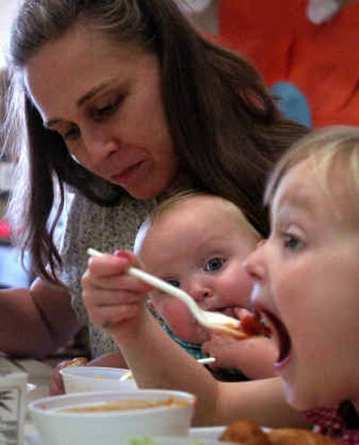 
Amelina Cox, 10 months, watches from the arms of her mother, Jennifer Cox as her sister Audrey Cox, 4, spoons a mouthful of lunch at The Enrichment Cooperative, where families are encouraged to participate in classes together. 
 (Jed Conklin / The Spokesman-Review)