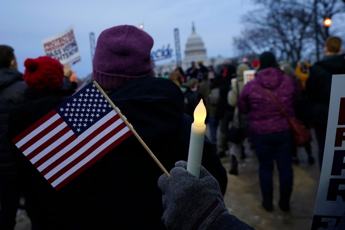 With the U.S. Capitol building in the background, a person holds an American flag and a flameless candle during a vigil Thursday in Washington, on the one-year anniversary of the attack on the U.S. Capitol.  (Julio Cortez)