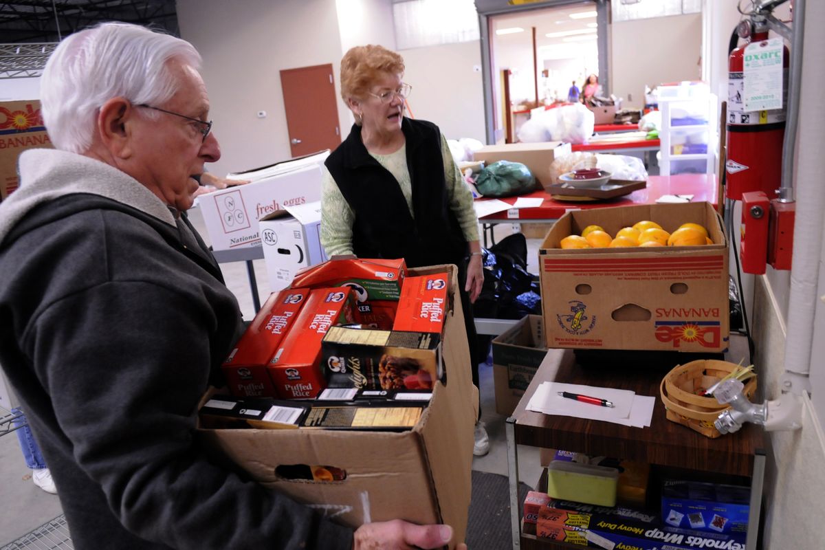 Spokane Valley Partners Food Bank volunteer Bob Mantle holds a box of food donated from Rosauers while food bank director Barb Bennett weights a box of oranges