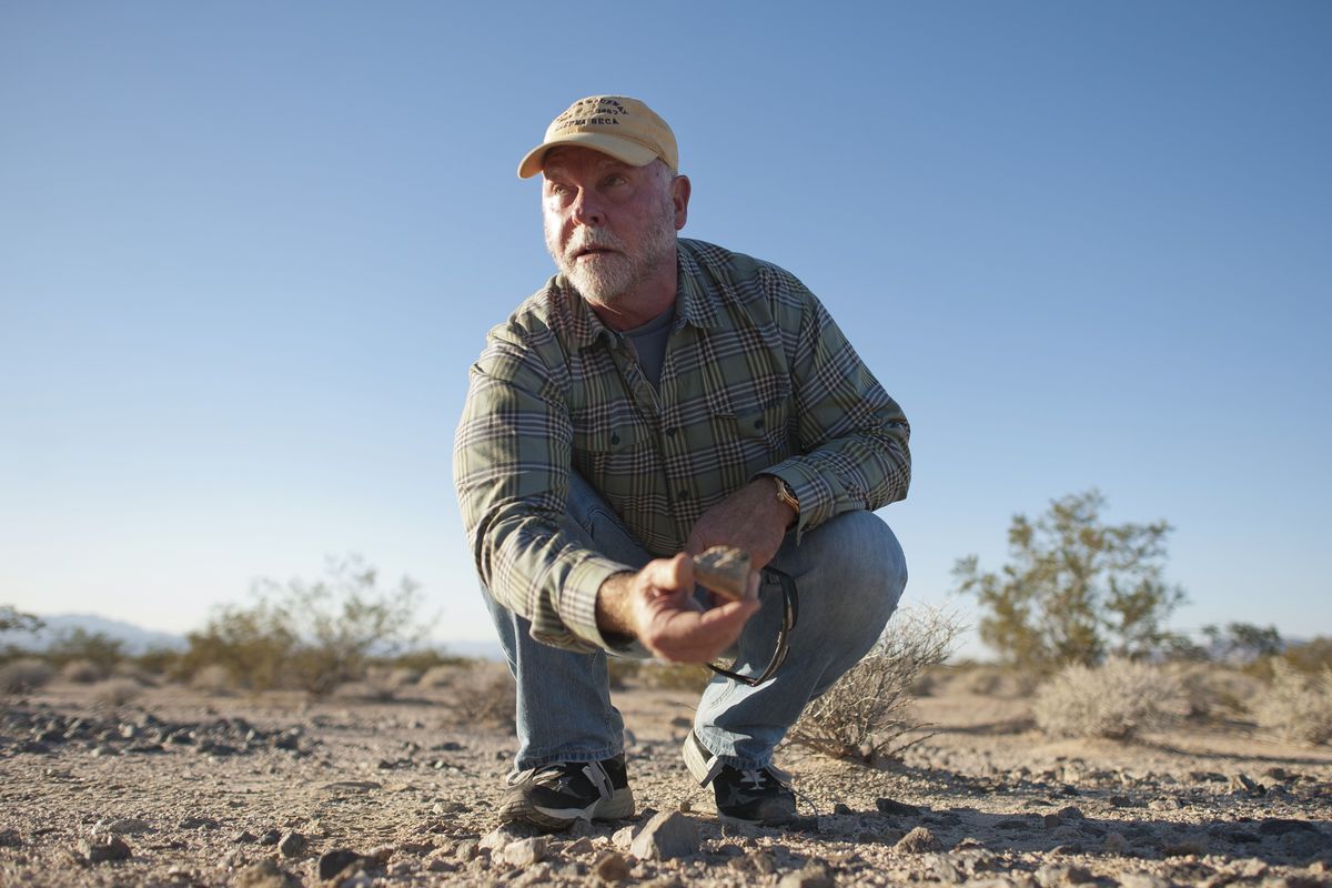 J. Craig Venter studies a rock at the location where his company, Synthetic Genomics, is preparing samples of soil and rock found in the Mojave Desert outside Baker, Calif., Nov. 15, 2013. Venter, a risk-taking outsider who brought speed, competition and controversy to the race to decode the human genome, died in San Diego on Wednesday, April 29, 2026. He was 79.   (Michal Czerwonka/The New York Times)