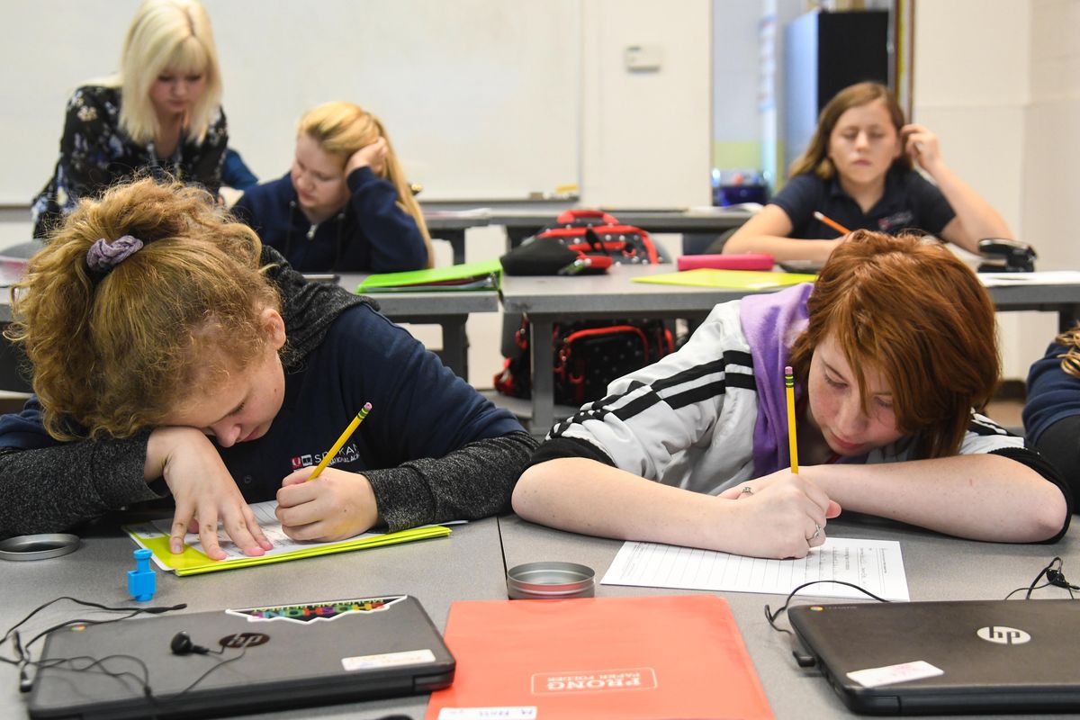 Spokane International Academy students Hailee Liedle, front left, and Madison Noll, right,  pore over an English assignment as teacher Kassie Sikes, top left, assists Jasmine Lane, with Evelyn Hall is at to right, Wednesday, Oct. 16, 2019. The Spokane International Academy is a charter school with about 500 students on two campuses.They recently purchased land up north that will allow them to merge the two buildings. (Dan Pelle / The Spokesman-Review)