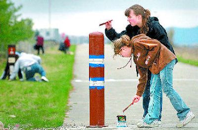 
Kalie Szablewski, 11, dips her brush into paint on Saturday while helping her sister, Jordan, paint a pole along the Centennial Trail near the state line. 
 (Brian Plonka / The Spokesman-Review)