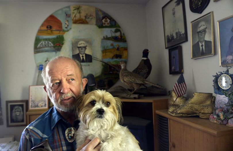 Flagpole painter Warren Hinrichs, 73, holds his dog Stitch and rests up at home in Spokane on Wednesday. He started climbing and painting flagpoles and water towers more than 50 years ago with his dad, Bill Hinrichs, seen in many photos in his home office. (Jesse Tinsley)
