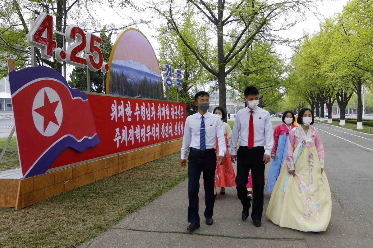 Citizens walk past celebrative posters displayed on the 90th founding anniversary of the Korean People