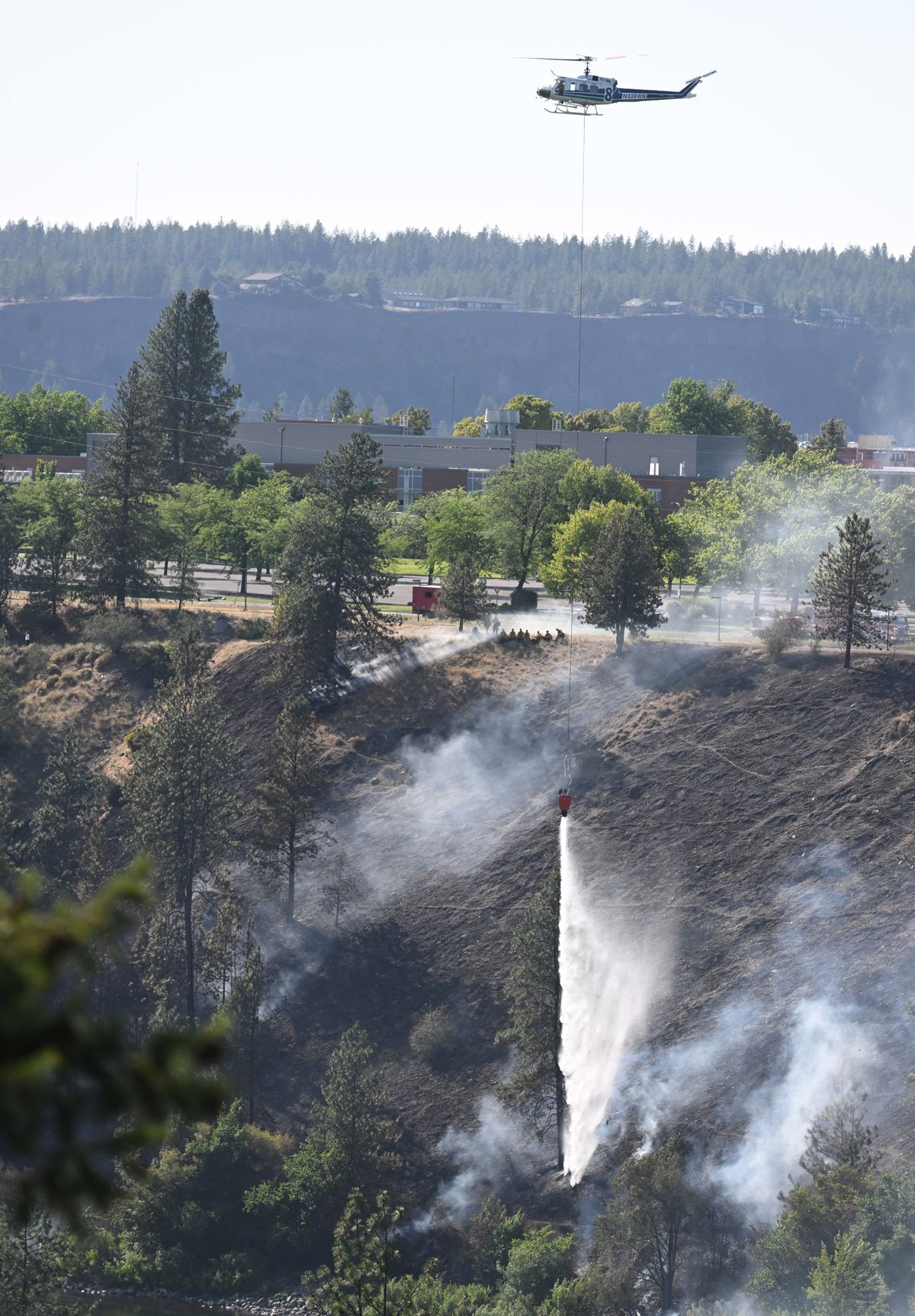 A helicopter from the Washington Department of Natural Resources drops a bucket of water onto the smoldering hillside near Spokane Falls Community College on Tuesday. The fire blackened the hillside and another suspicious fire also started just a few hundred yards away.  (Jesse Tinsley/THE SPOKESMAN-REVIEW)