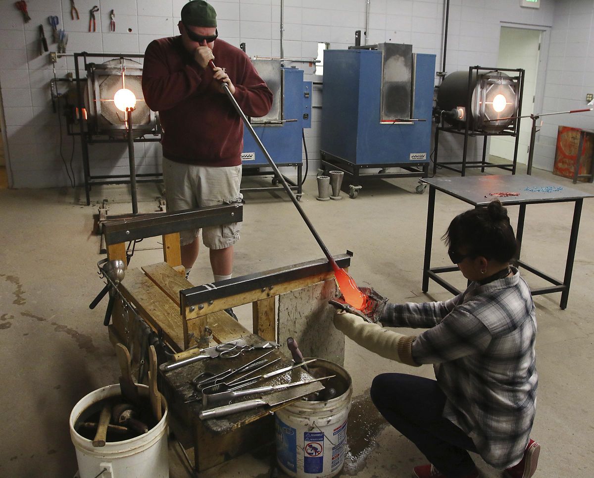 River Newman blows into a pipe holding a blob of molten glass Jan. 19, creating a bubble to start a vessel as assistant and Butte High School senior Janae Valle uses wet newspaper to shape the cylinder, in Butte, Mont. Newman is a traveling elementary art teacher for the Butte school district. (Walter Hinick / Photos by Walter Hinick / Montana Standard)