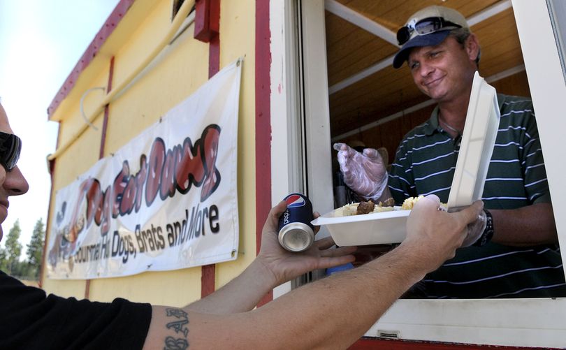 Dog Eat Dawg owner Van Austin hands a plate of food to regular customer Davis Shutts, of Coeur d’Alene, from his mobile eatery on the corner of Seltice Way and Atlas Road in Coeur d’Alene on Thursday. Part of their proceeds are donated to the Kootenai Humane Society. (Kathy Plonka / The Spokesman-Review)