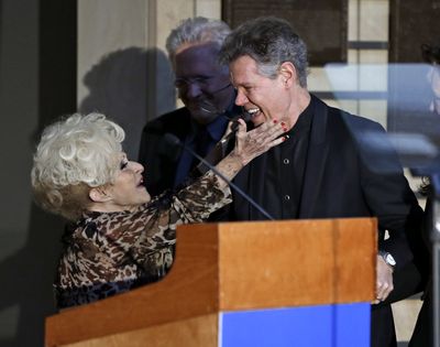 Country music singer Randy Travis is embraced by emcee, Brenda Lee,  left, at a press conference announcing inductees, Travis, fiddler Charlie Daniels and producer and label owner Fred Foster to the Country Music Hall of Fame in Nashville, Tenn., on Tuesday, March 29, 2016. (Mark Humphrey / Associated Press)