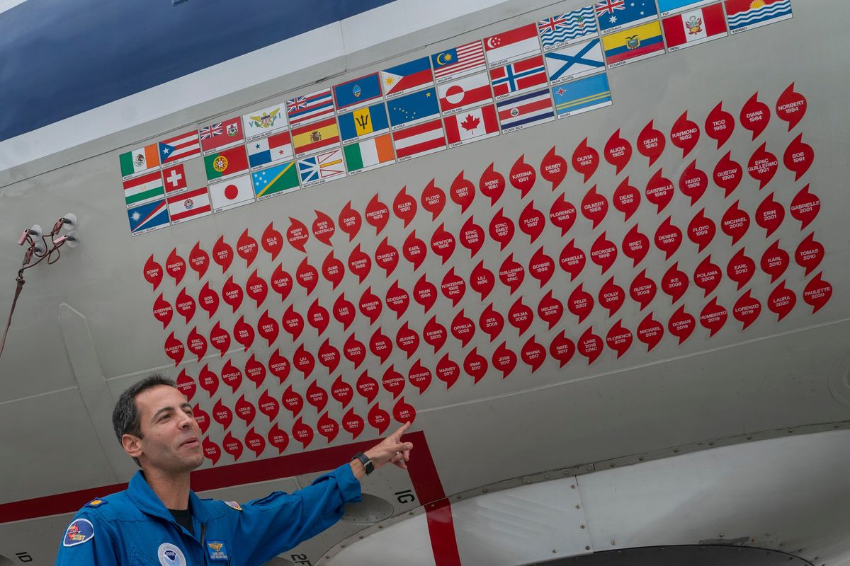 Lt. Commander Sam Urato, a P-3 pilot of National Oceanic and Atmospheric Administration, points to decals on the fuselage of the Lockheed WP-3D Orion 