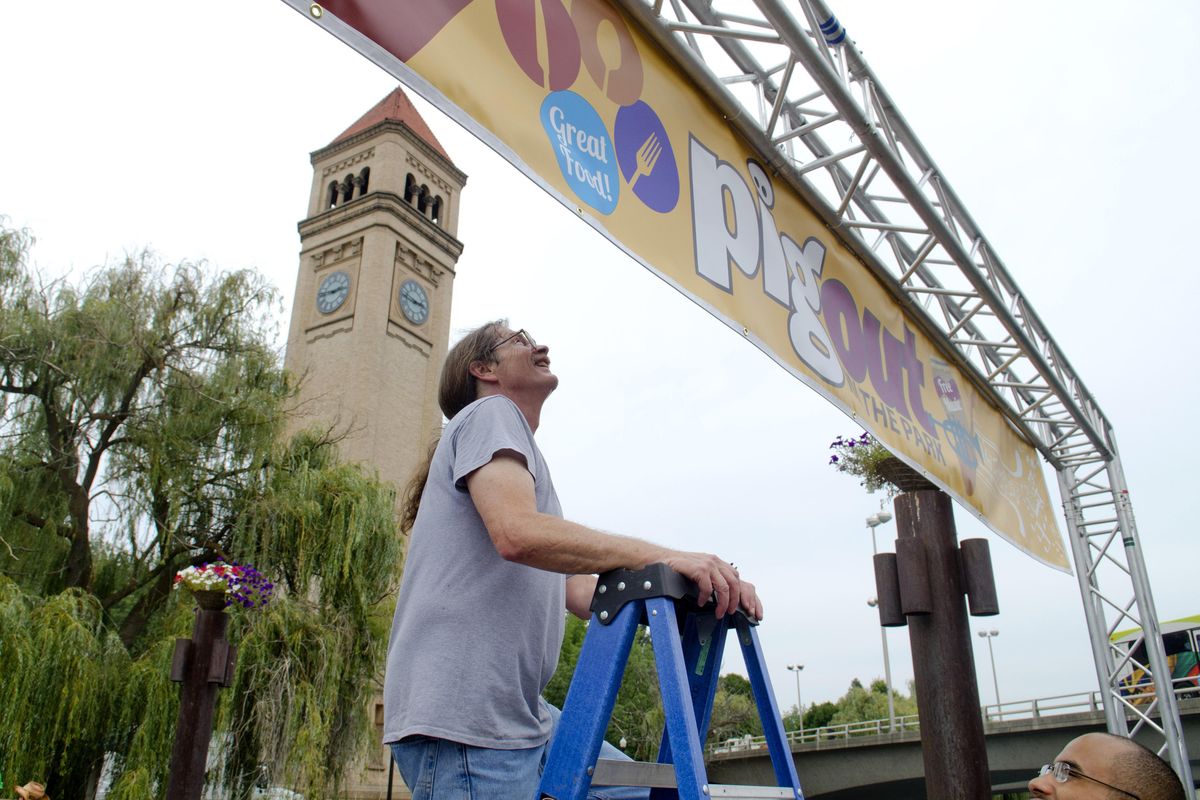 Bill Burke, longtime organizer of Pig Out In The Park food and music festival, finishes hanging the last of three banners on a foot bridge across the south channel of the Spokane River leading to the Clocktower Meadow in Riverfront Park Tuesday, Aug. 30, 2016. "This (bridge) is something we