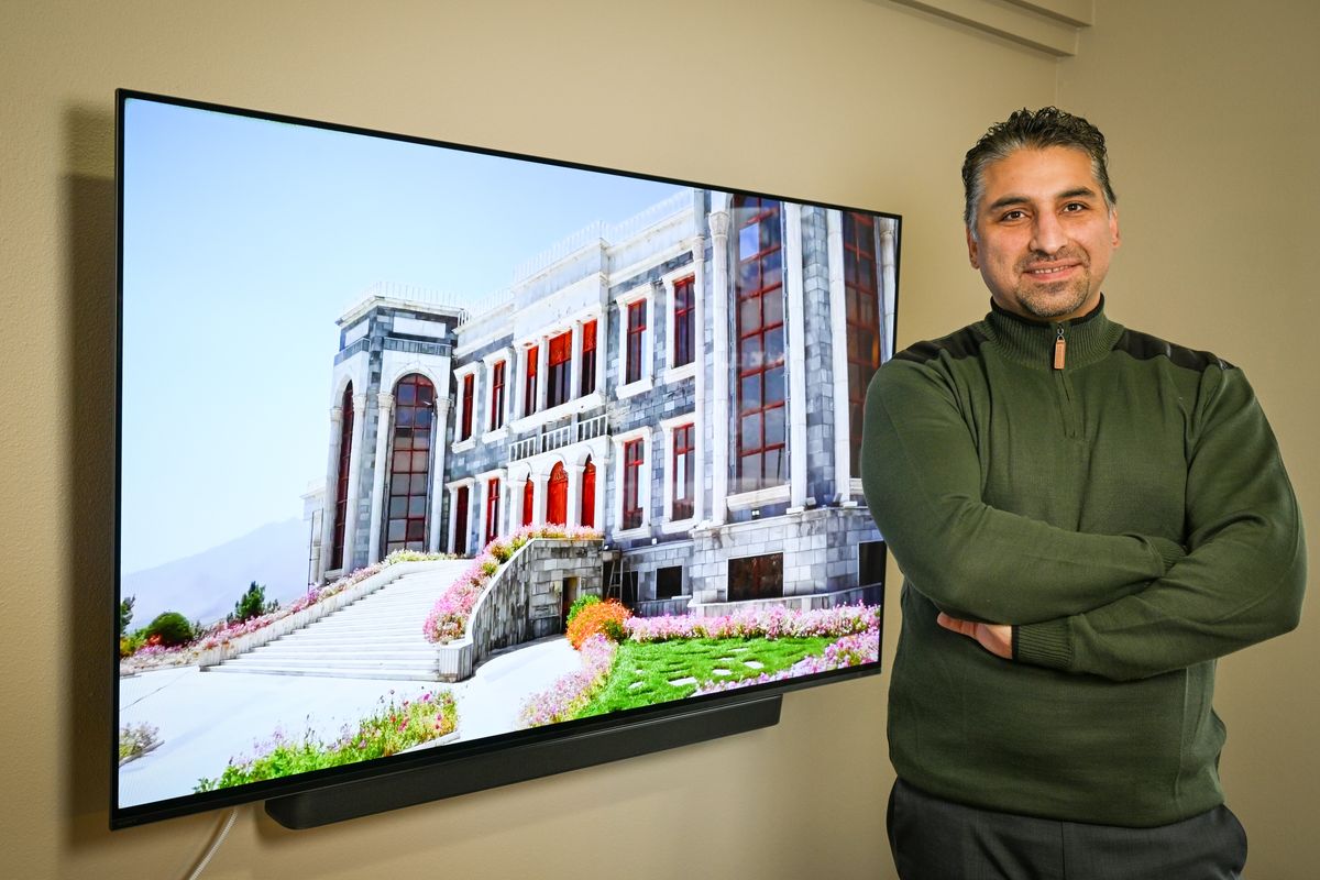 Kazim Abdullahi, an immigrant from Afghanistan who is now a naturalized U.S. citizen, stands in his home Friday in Spokane. Behind him on the television is a YouTube image of the presidential palace in Afghanistan.  (Jesse Tinsley/THE SPOKESMAN-REVIEW)
