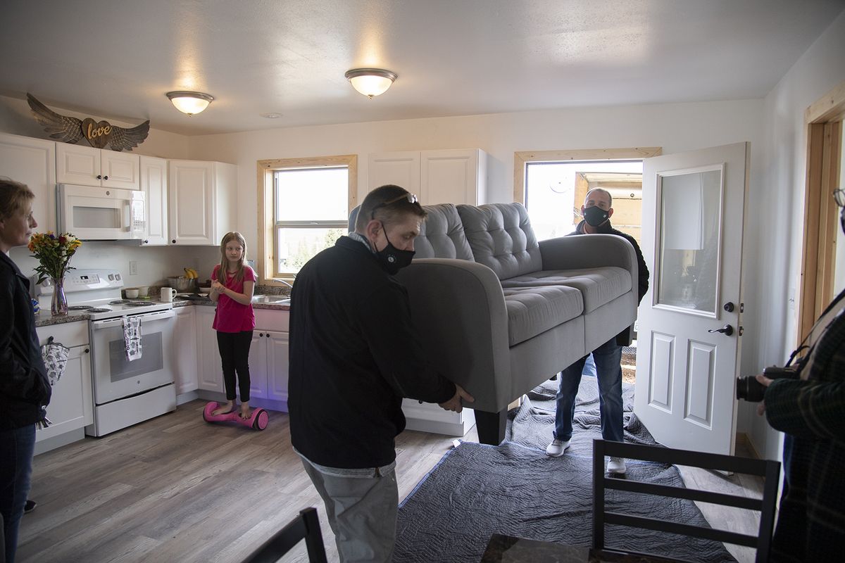 Diana Totten, far left, and her daughter Briaunna Totten,12, watch as furniture is hauled into the new home built for them in Malden, Washington Friday, Mar. 26, 2021. The new home was just completed my missionaries of an Anabaptist community from Montana. Carrying the new couch is Tennessee Cochran, center, and Jason McSteen, owner of furniture store 16 Cents, 3 Shoes & 5 Socks.  (Jesse Tinsley/The Spokesman-Review)