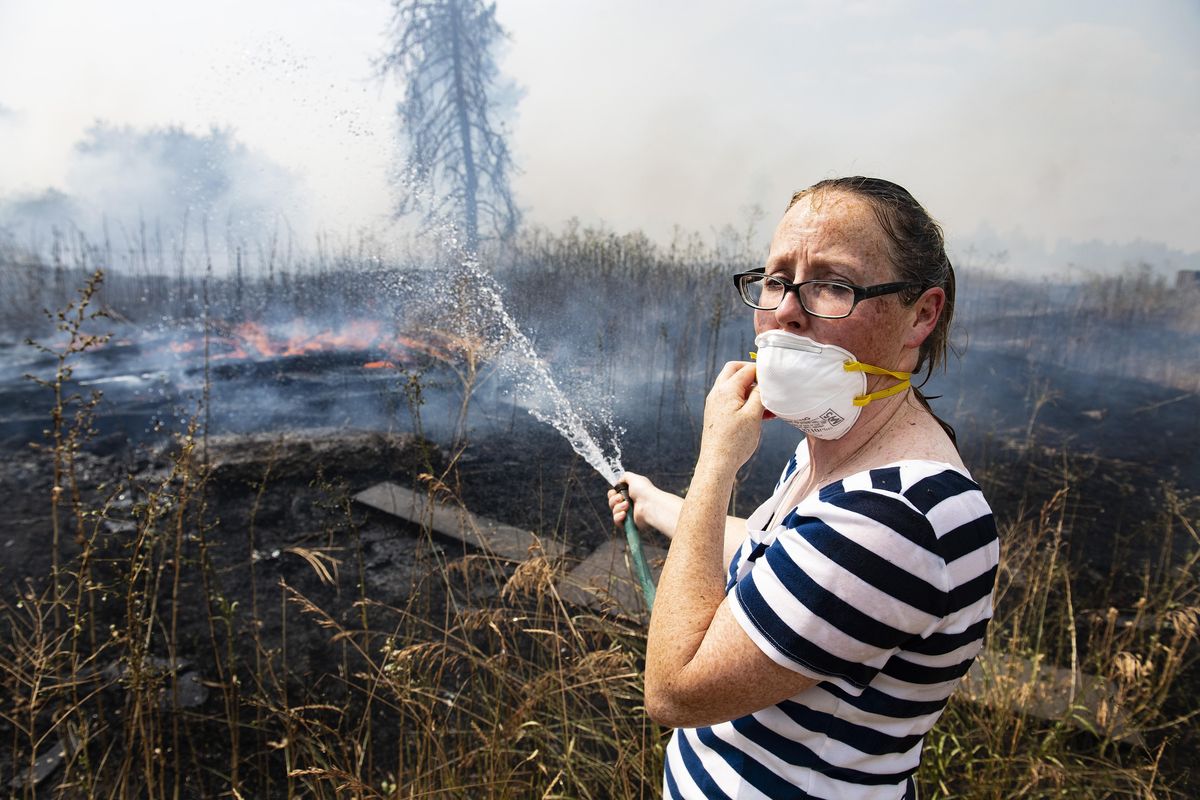 Vonae Nielson, soaked head to toe from an air water drop, uses a garden hose to put out hot spots behind her home on South Granite Lake Road, near Cheney Wash., Mon., Aug. 6, 2018, A fast-moving brush fire quickly grew to 100 acres and its smoke forced brief closures on Interstate 90 in both directions near the Cheney exit as fire officials called for the evacuations of up to 100 nearby homes. (Colin Mulvany / The Spokesman-Review)