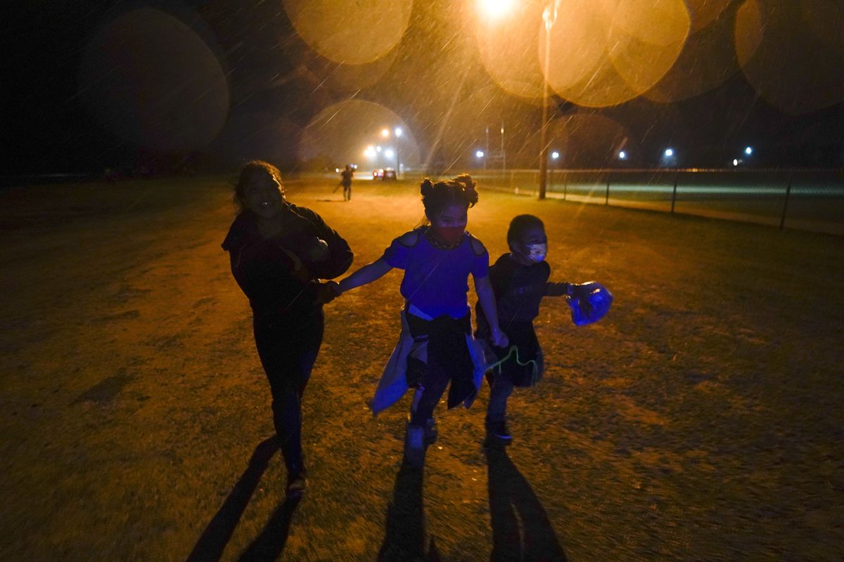 In this May 11, 2021 photo, three young migrants hold hands as they run in the rain at an intake area after turning themselves in upon crossing the U.S.-Mexico border in Roma, Texas. Five months after the Biden administration declared an emergency and raced to set up shelters to house a record number of children crossing the U.S.-Mexico border alone, kids continue to languish at the sites, while more keep coming, child welfare advocates say.  (Gregory Bull)