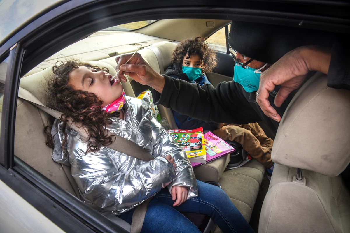 Adams Elementary School first-grade student Rita Mae Burnley, 6, gets a mouth swab from her father, Michael Burnley, during curbside COVID-19 testing in January at Chase Middle School in Spokane. Kindergarten student Jerome Burnley, 5, in the back seat with his sister, waits for his turn.  (Dan Pelle/THESPOKESMAN-REVIEW)