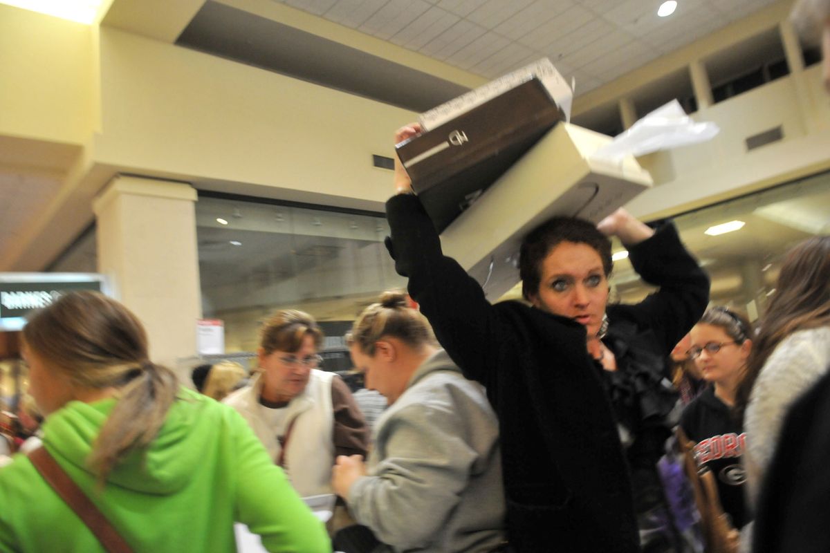 A shopper holds boxes of boots above her head as she makes her way through a crowd during Black Friday shopping at a Belk store in Oglethorpe Mall in Savannah, Ga. on Friday, Nov. 23, 2012. (Richard Burkhart / The Savannah Morning News)